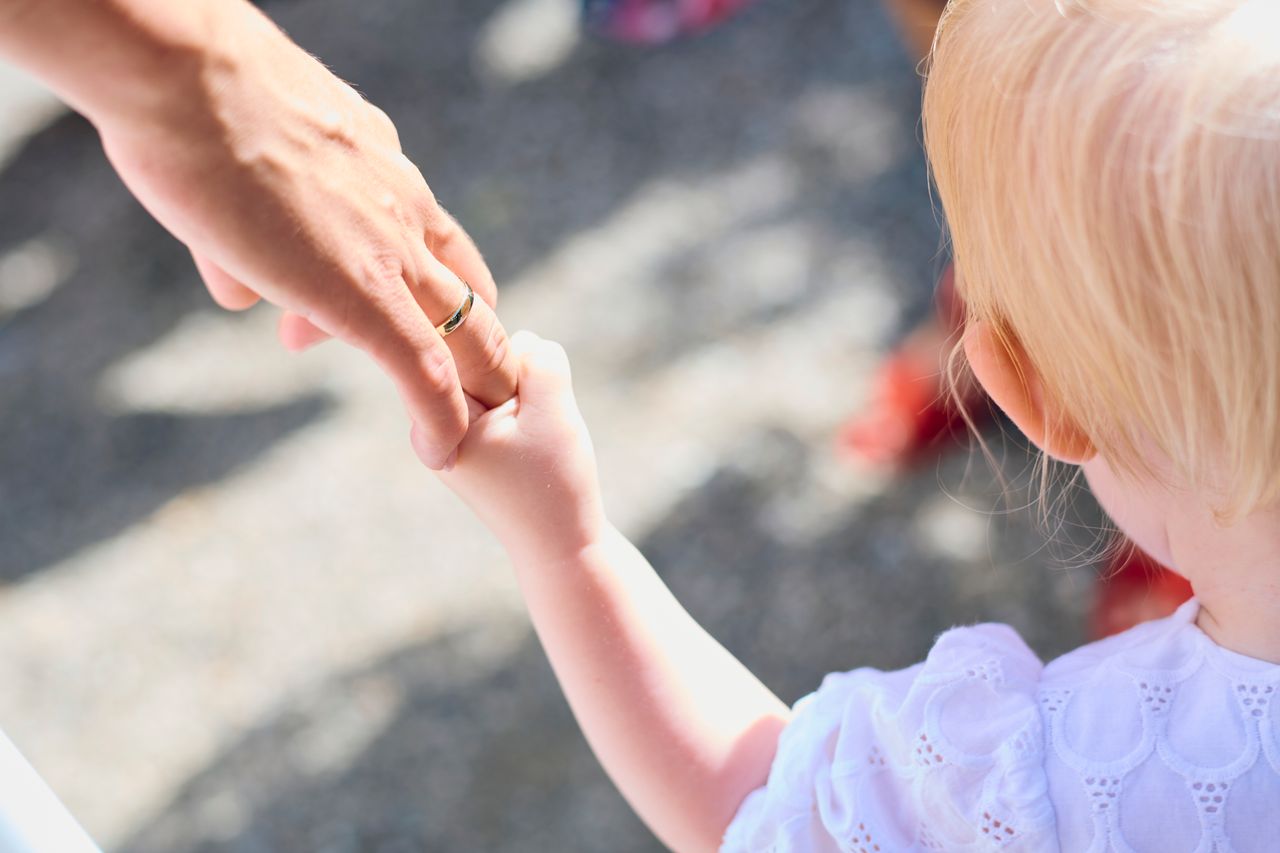 Blonde child holding parent's hand outdoors, symbolizing love and protection.