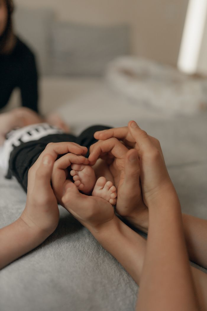 Close-up of adult and child hands gently holding baby feet, creating a heart shape.