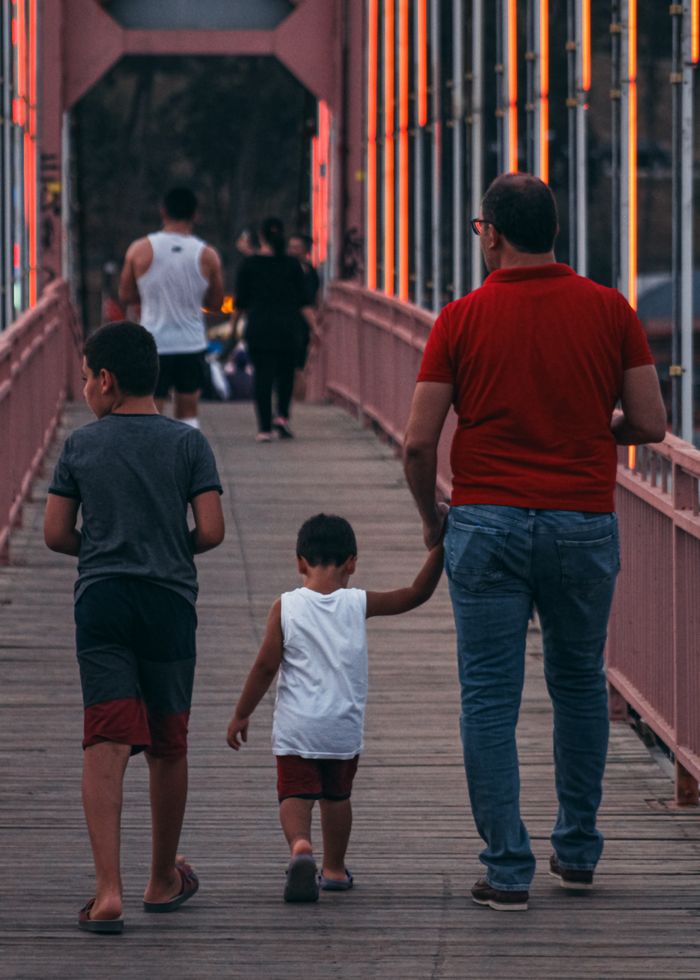 Father and two sons walking on a colorful footbridge at dusk, bonding and family time.
